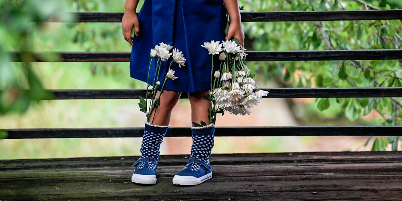 A single image of a young girl wearing a Footmates "Drew" vulcanized sneaker shoe.  "Taylor", "Jordan", "Drew", and "Reese" are the names for the available Footmates sneaker patterns.  There is a clickable link in the bottom right corner of the image to "Shop Footmates Sneaker Shoes".